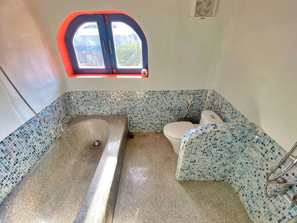 Een badkamer met een badkuip, toilet en raam met een rode omlijsting.