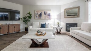 A modern living room with a white sofa, a coffee table, a fireplace, and abstract art on the wall. - Cozy Modern Home! (Vancouver)