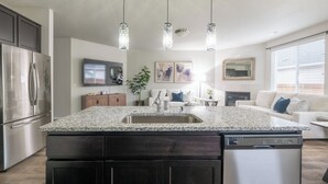 A modern kitchen with granite countertops, stainless steel appliances, and pendant lighting. - Cozy Modern Home! (Vancouver)