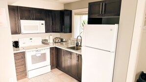 Een moderne keuken met donkere houten kastjes, een witte koelkast, een magnetron, een fornuis en een spoelbak.
