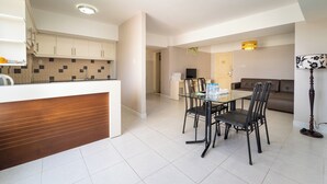 A modern kitchen with white cabinets, a wooden countertop, and a dining area with a glass table and black chairs. - Palette Muine Boutique Hotel Near Mui Ne Beach (1 Bao Loc)