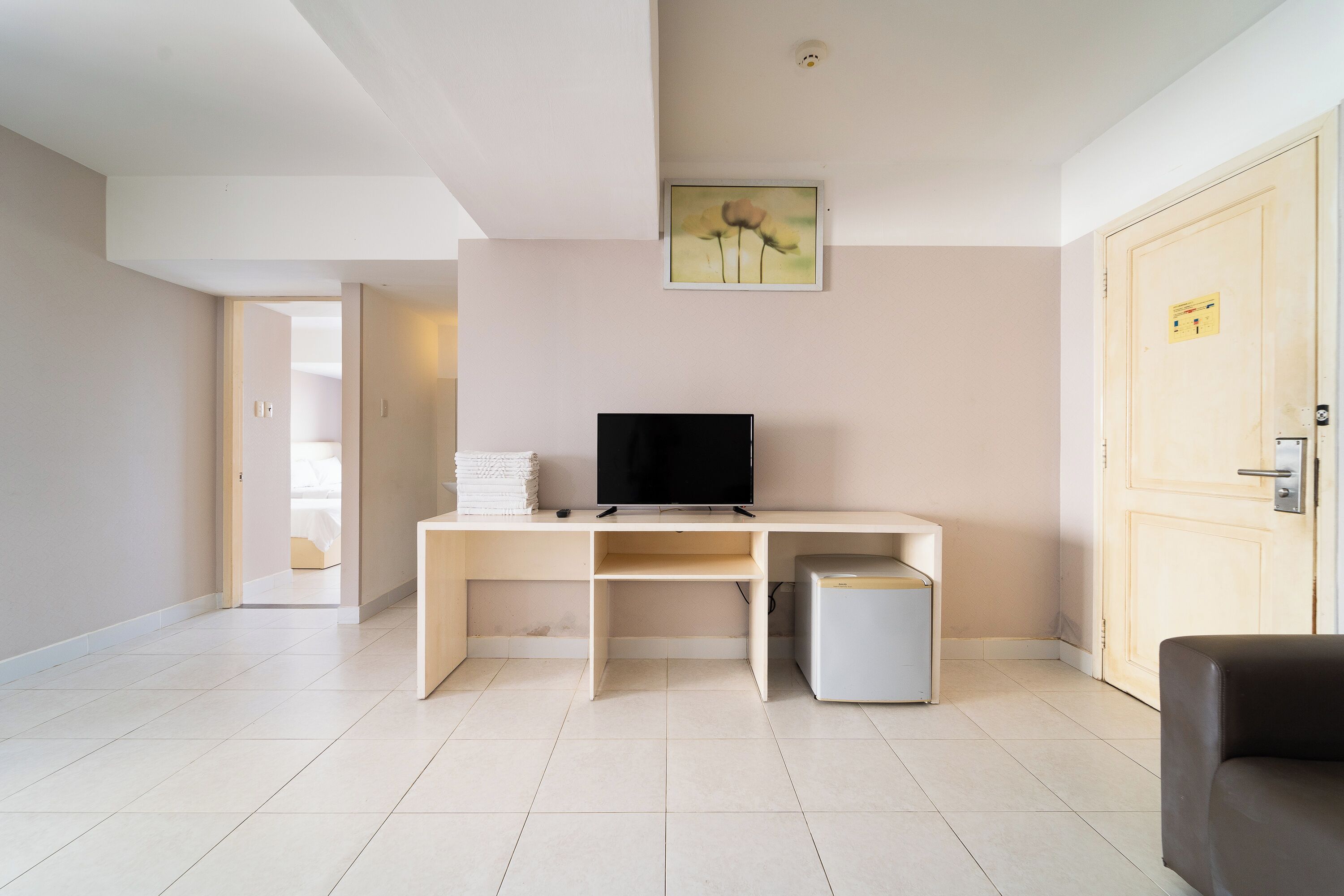 A modern room with a desk, a television, a small refrigerator, and a door.