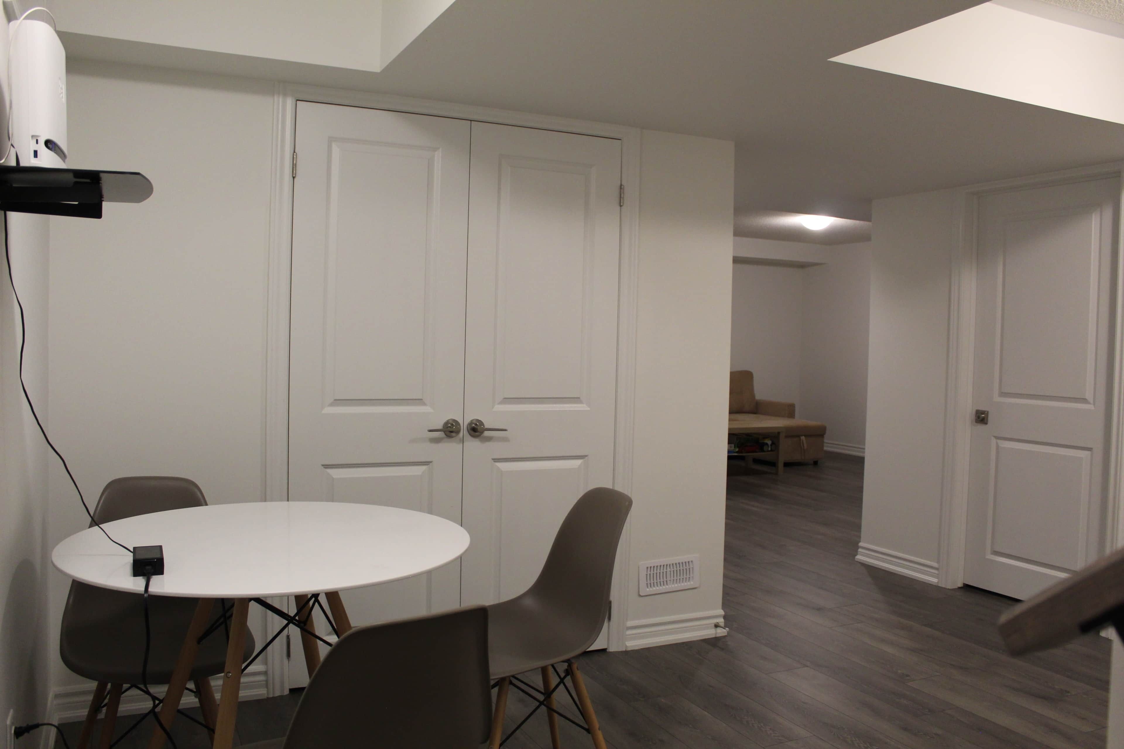 Una habitación con una mesa redonda blanca, dos sillas, un armario blanco y suelo de madera.