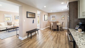 A spacious living area with a dining table and chairs, a bench, and a kitchen with a granite countertop and cabinets.