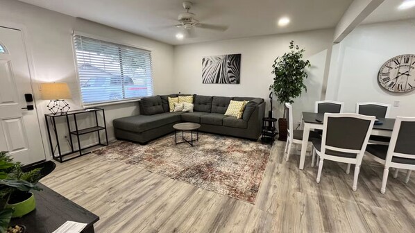 A modern living room with a sectional sofa, a dining table with chairs, a coffee table, a large clock, and a ceiling fan. - Only 5 min to ASU! (Tempe)