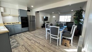 A modern kitchen with grey cabinets, a stainless steel refrigerator, and a dining area with white chairs and a table. - Only 5 min to ASU! (Tempe)