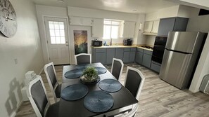 A modern kitchen with grey cabinets, a stainless steel refrigerator, and a dining table with placemats and chairs. - Only 5 min to ASU! (Tempe)