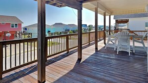 A wooden deck with a railing, two Adirondack chairs, and a view of houses in the background. - Under the Sea (Galveston)