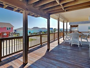 A wooden deck with a railing, two Adirondack chairs, and a view of houses in the background. - Under the Sea (Galveston)