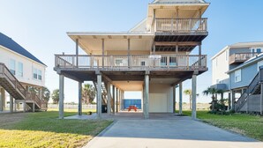 A two-story building with a balcony on the upper level, a covered area on the ground floor, and a visible garage door. - Under the Sea (Galveston)