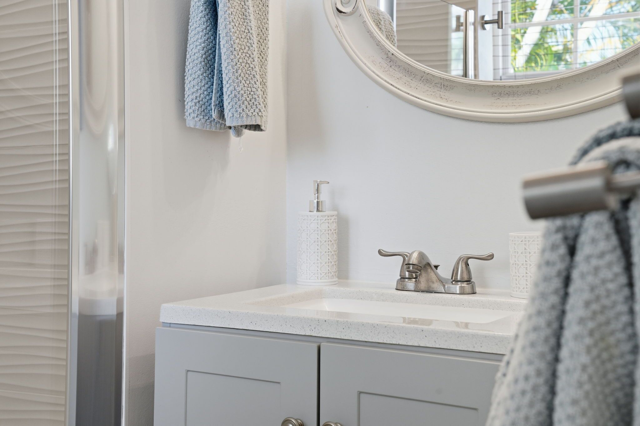 Une salle de bain avec un lavabo blanc, un miroir rond et un porte-serviettes avec deux serviettes.
