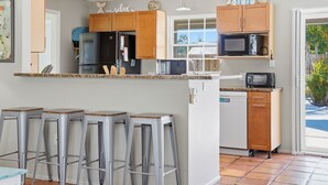 A kitchen with wooden cabinets, a refrigerator, a microwave, and a dishwasher. There are four bar stools and a window with a view of the outdoors. - ⚓Private Heated Pool & Minutes to Anna Maria Island!⚓ (Bradenton)