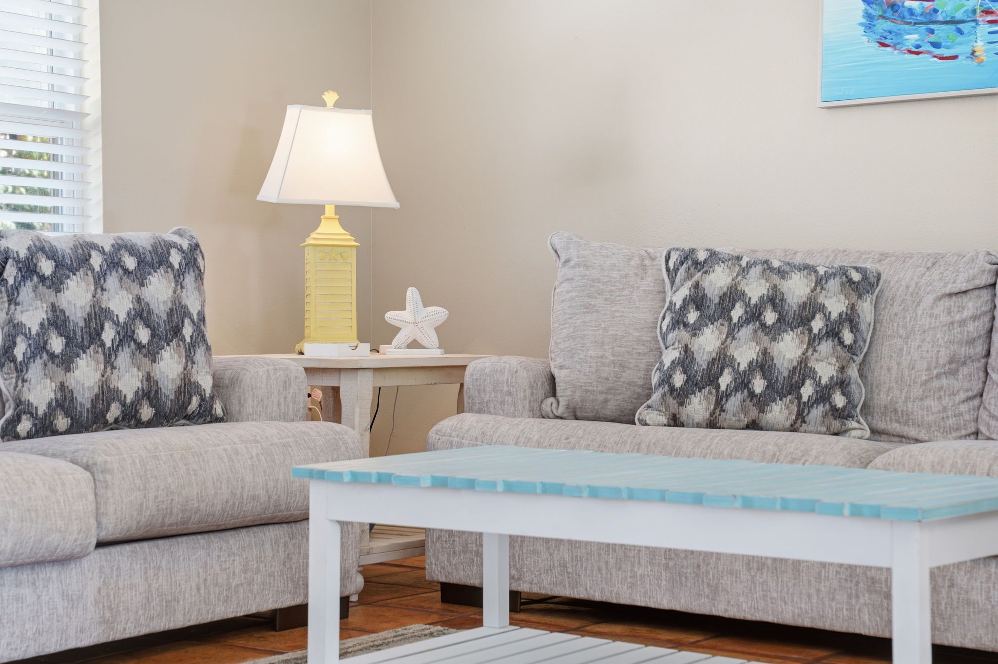 A living room with two grey sofas, patterned cushions, a white table, a yellow lamp, and a starfish decoration.
