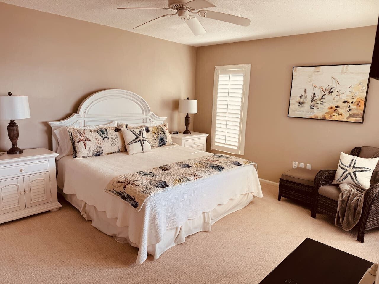 A bedroom with a bed, nightstands, a chair, a ceiling fan, and a painting on the wall.
