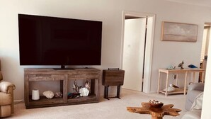 Un salon moderne doté d’un téléviseur à écran plat, d’un meuble de rangement en bois, d’un canapé en cuir et d’un ventilateur de plafond.
