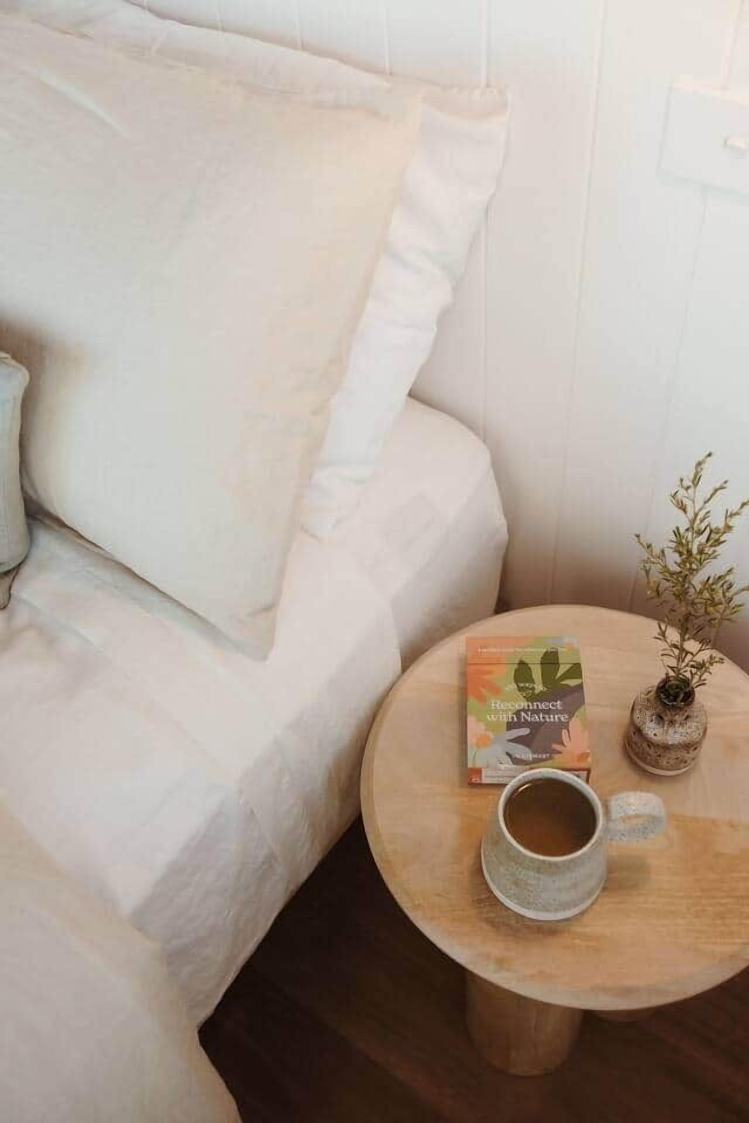 Ein gemütliches Zimmer mit einem weißen Sofa, einem runden Holztisch mit einem Buch und einer Tasse sowie einer kleinen Topfpflanze.