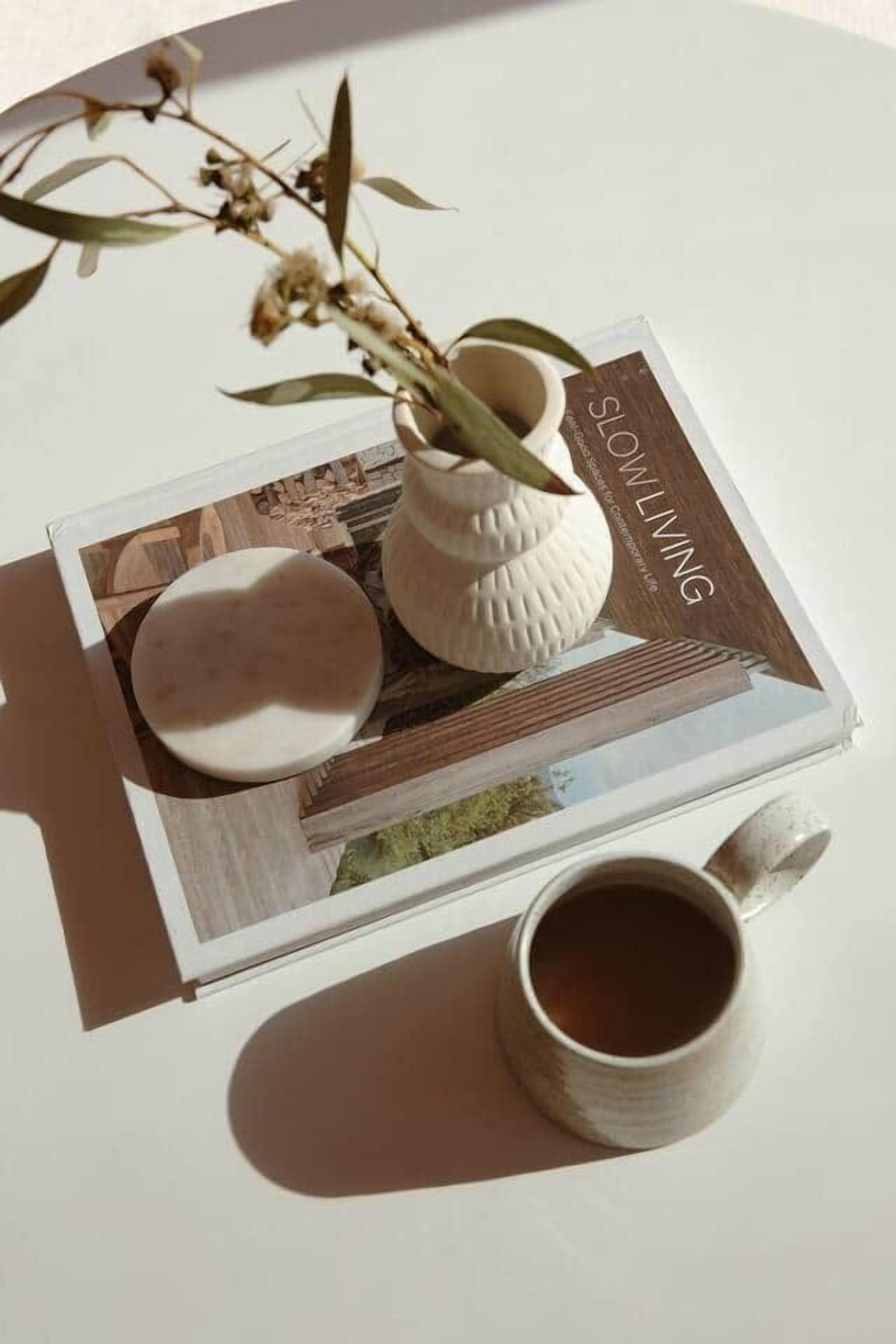 Ett bord med ett tidningsnummer, en keramisk mugg och en liten vas med torkade blommor.