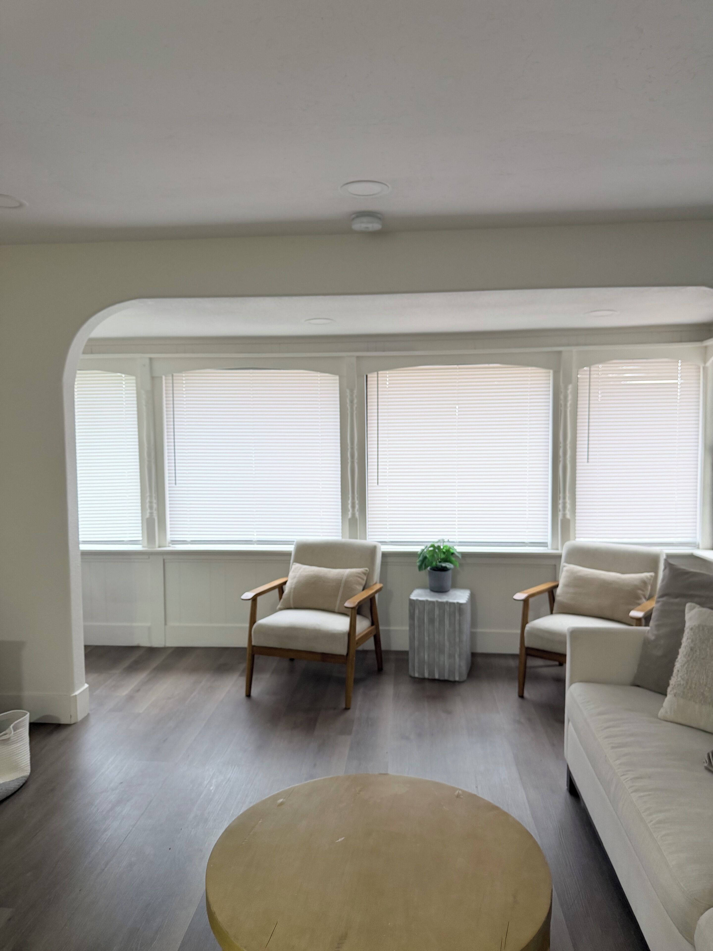 Ein geräumiges Wohnzimmer mit großem Fenster, zwei Sesseln, einem runden Couchtisch und einer Couch.