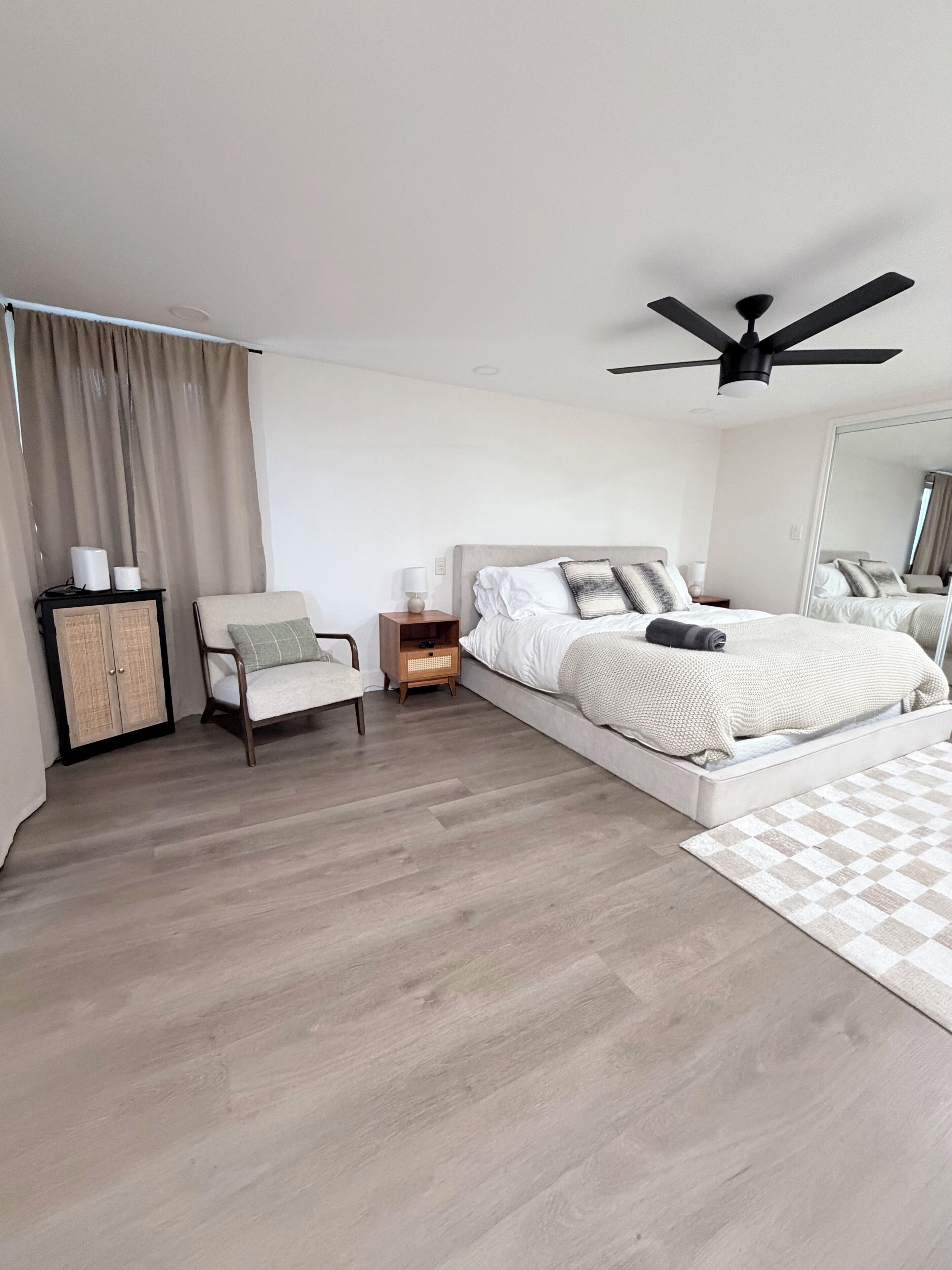 Een moderne slaapkamer met een bed, een stoel, een nachtkastje, een plafondventilator en een kledingkast.