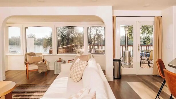 Un salon spacieux, doté d’un grand canapé, d’une table basse et offrant une vue sur un lac grâce à de grandes fenêtres.