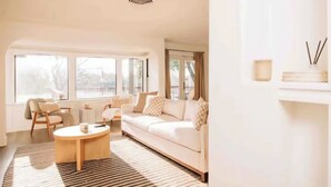 Un salon spacieux avec un canapé blanc, une table basse ronde et une grande fenêtre offrant une vue sur l’extérieur.