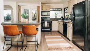 Une cuisine moderne avec un réfrigérateur noir, deux chaises orange, un four à micro-ondes et une cuisinière.