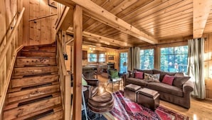A wooden interior with a staircase, a living room with a sofa and ottoman, and large windows. - Creekside Old Tahoe style meets modern cozy Zen Den (Tahoe City)
