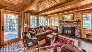 A cozy cabin interior with a stone fireplace, wooden beams, a large window, and a comfortable seating area. - Creekside Old Tahoe style meets modern cozy Zen Den (Tahoe City)