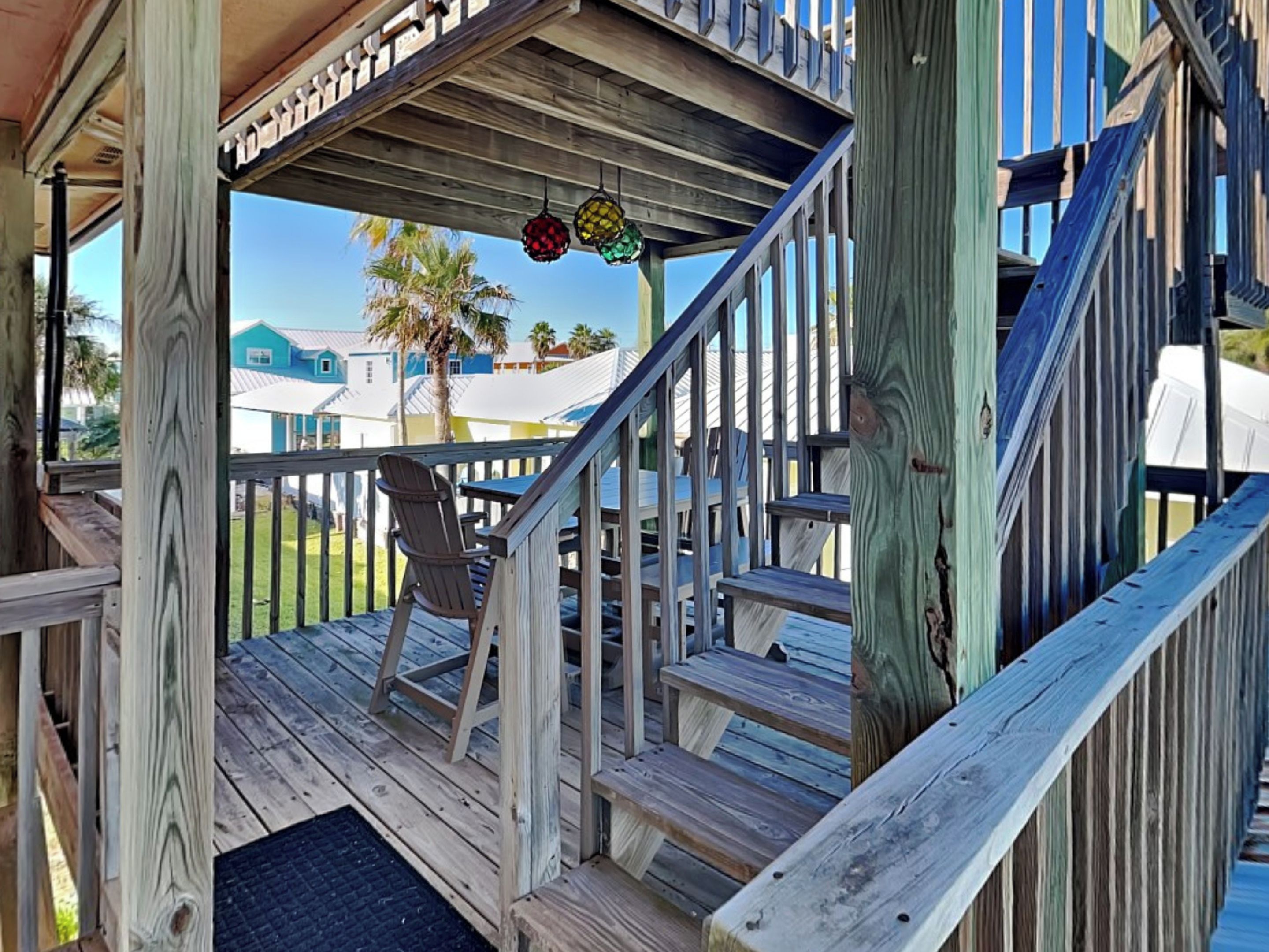 A wooden deck with a chair and a staircase leading to a covered area.