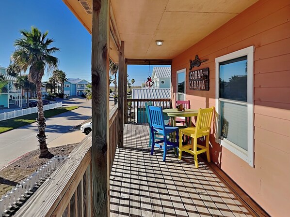 A balcony with a tiled floor, a table, and colorful chairs.