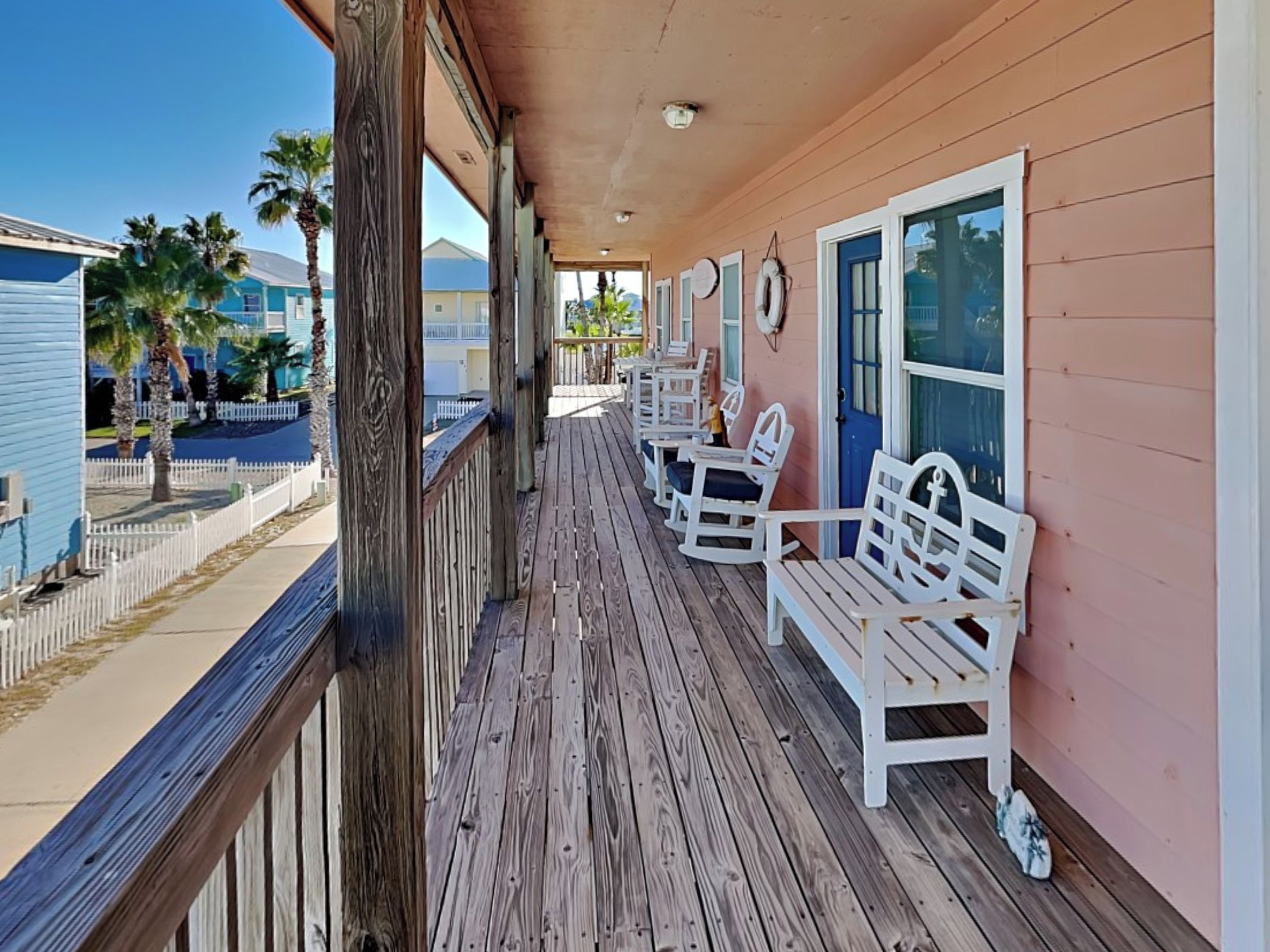 A wooden porch with white rocking chairs and a pink wall.