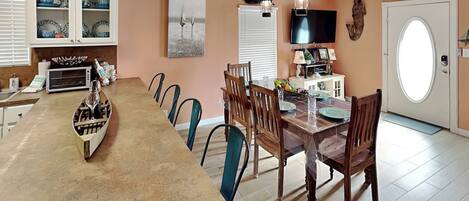 A dining area with a long table, chairs, a chandelier, and a television.