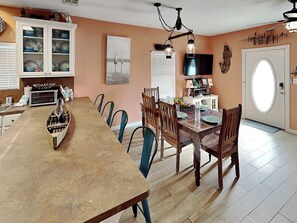 A dining area with a long table, chairs, a chandelier, and a television.