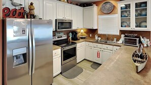 A modern kitchen with white cabinets, stainless steel appliances, and a wooden countertop. - Coral Cabana (Port Aransas)