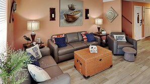 A living room with a sofa set, a wicker coffee table, and a painting of boats on the wall. - Coral Cabana (Port Aransas)