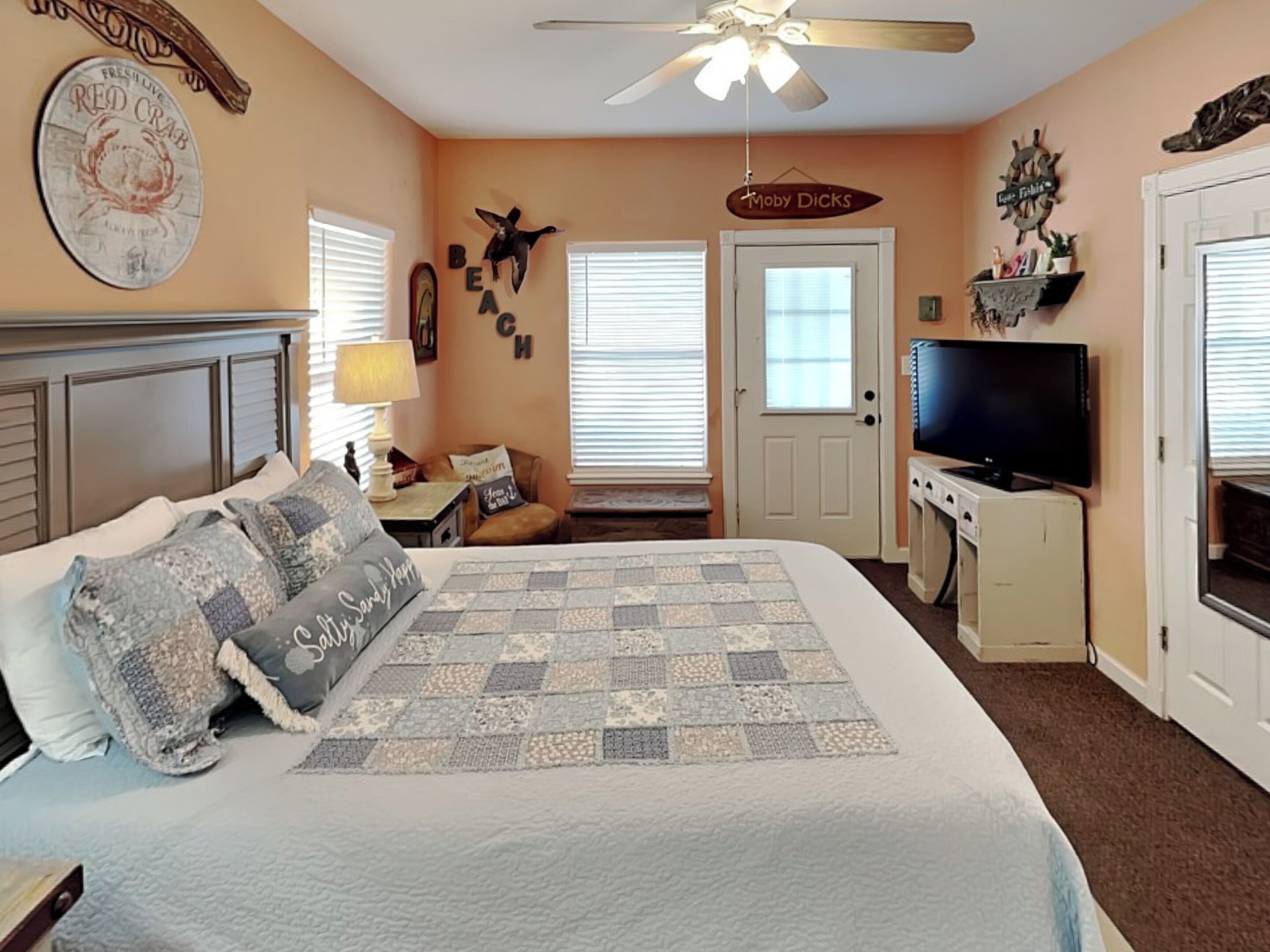 A bedroom with a bed, a television, a ceiling fan, and a door.