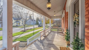 A covered porch with a wooden railing, a hanging light fixture, and a bench. - Soul of SoHa, a spacious 5-bedroom retreat in South Haven, MI. (South Haven)