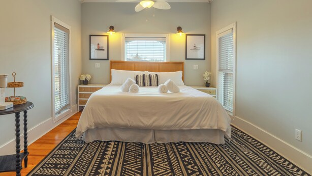 A bedroom with a bed, a ceiling fan, a window with blinds, and a patterned rug. - Soul of SoHa, a spacious 5-bedroom retreat in South Haven, MI. (South Haven)