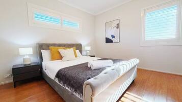 A bedroom with a bed, nightstands, a window, and a wall-mounted artwork.