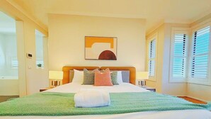 Quarto de hotel com cama grande, cabeceira, mesa de cabeceira com abajur e obra de arte na parede.