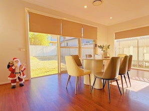 A spacious dining area with a round table and modern chairs, large sliding glass doors leading to a yard, and a small Santa figurine on the floor.