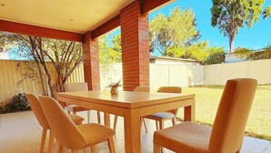 Um pátio externo com mesa de madeira e quatro cadeiras.