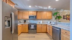 A modern kitchen with wooden cabinets, stainless steel appliances, granite countertops, and a built-in oven. - Heart of Helen - 1st Floor | Walk to Main Square (Helen)