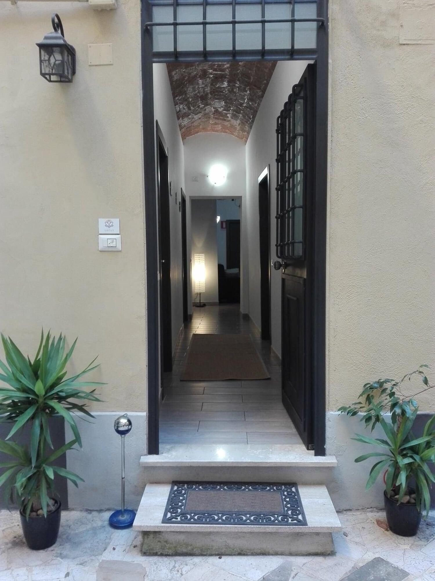 A narrow hallway with a metal gate at the entrance, a doormat, and potted plants on either side.