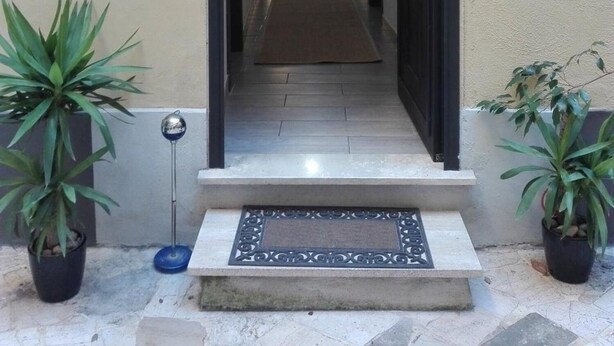 A narrow hallway with a metal gate at the entrance, a doormat, and potted plants on either side. - Maison Villa Torlonia (Rome)