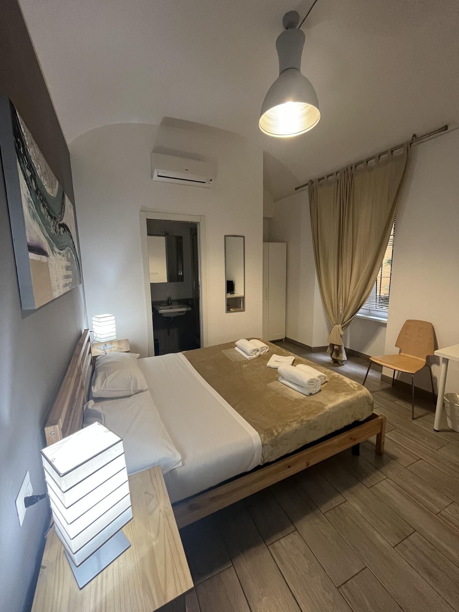 A hotel room with a bed, bedside table, lamp, and a view of the bathroom.