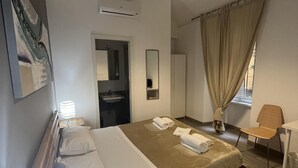 Una camera d'albergo con un letto, un comodino, una lampada e vista sul bagno.