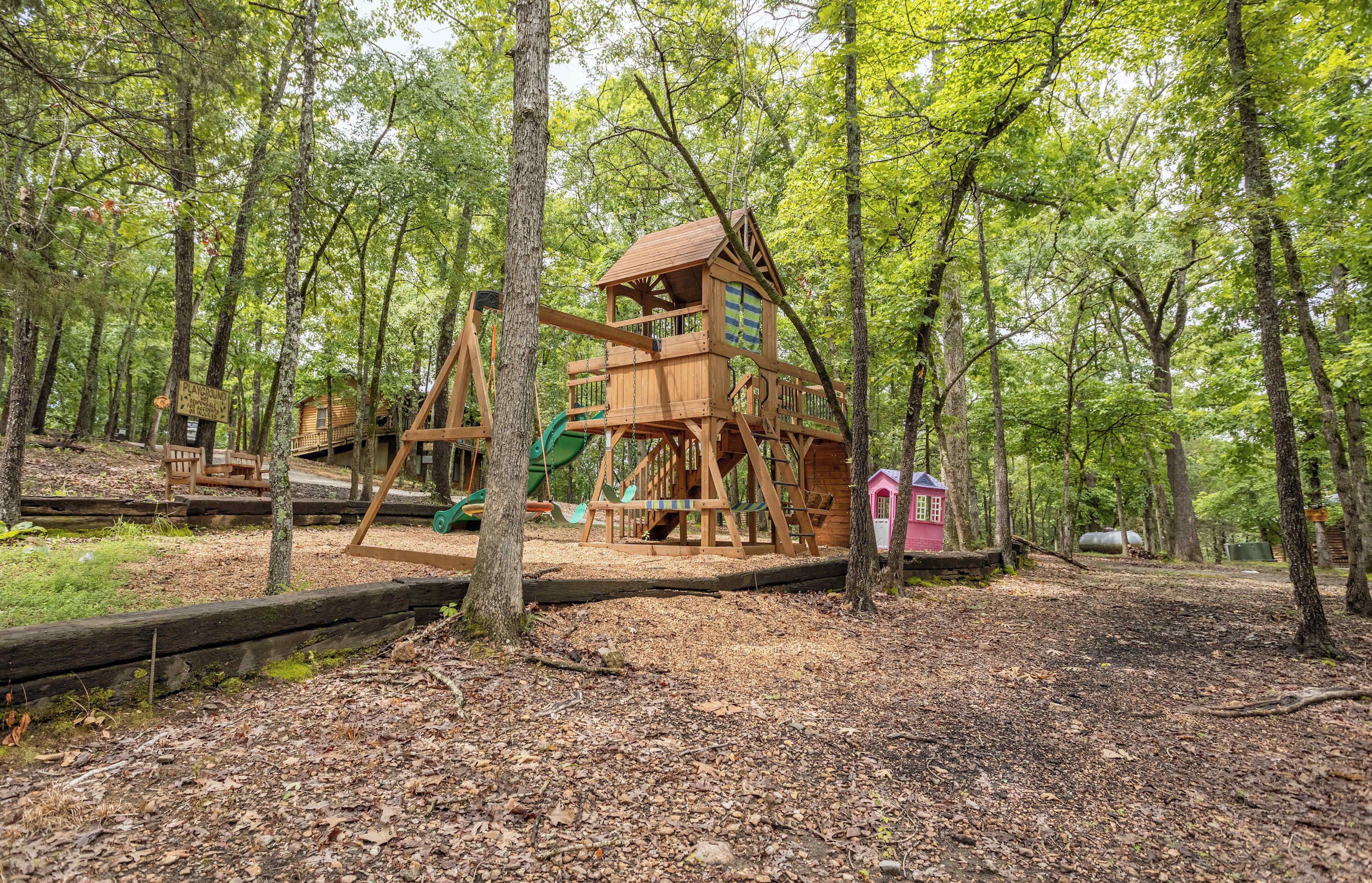 A wooden play structure in a forested area with a slide and a small building.