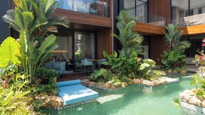 Uma área de piscina moderna ao ar livre, com plantas tropicais exuberantes, um deck de madeira e um espaço de estar com cadeiras e uma mesa.