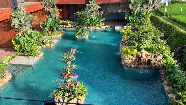 Um edifício moderno com piscina, rodeado por plantas tropicais e uma pequena cascata.